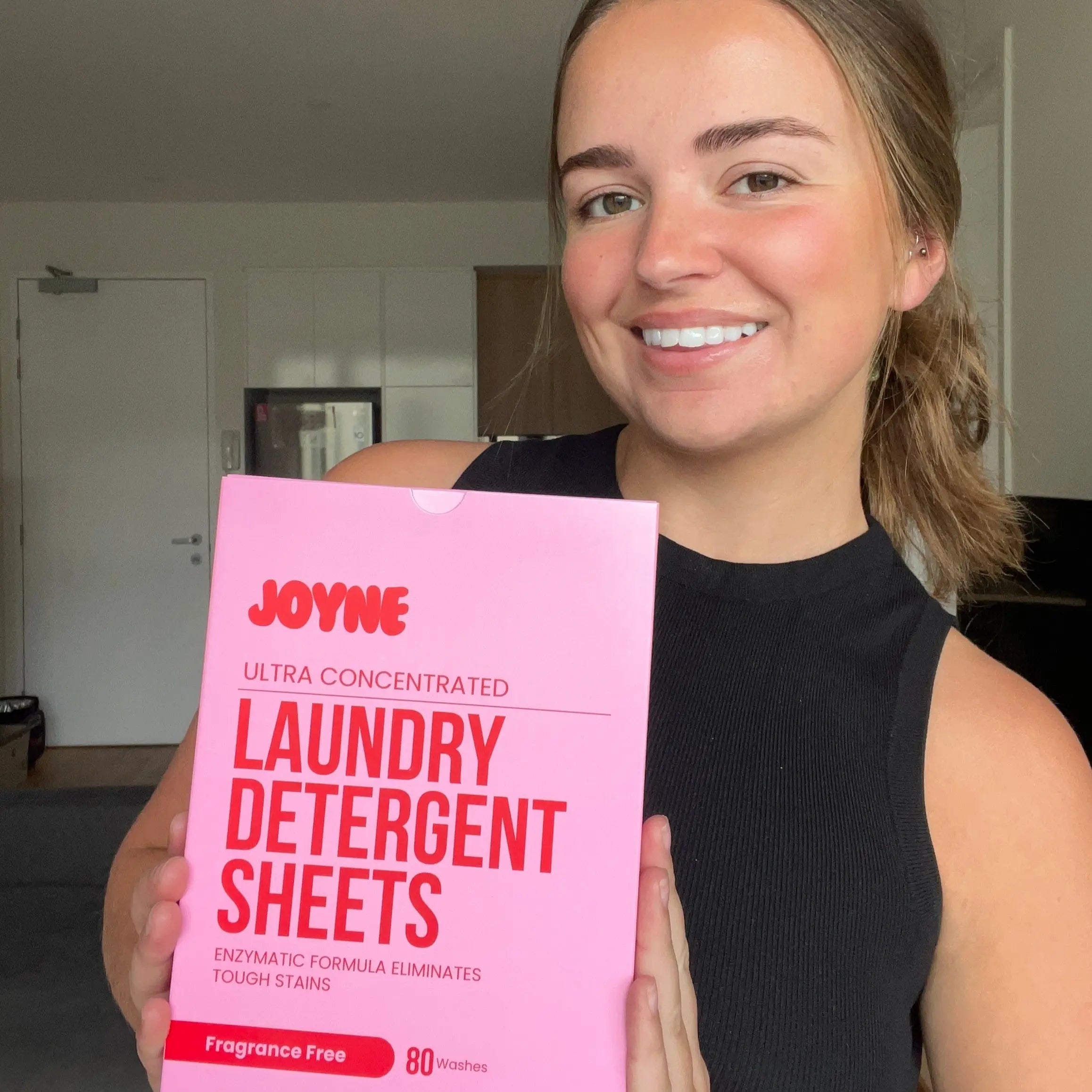 A female customer smiling and holding a pink box of JOYNE laundry detergent sheets