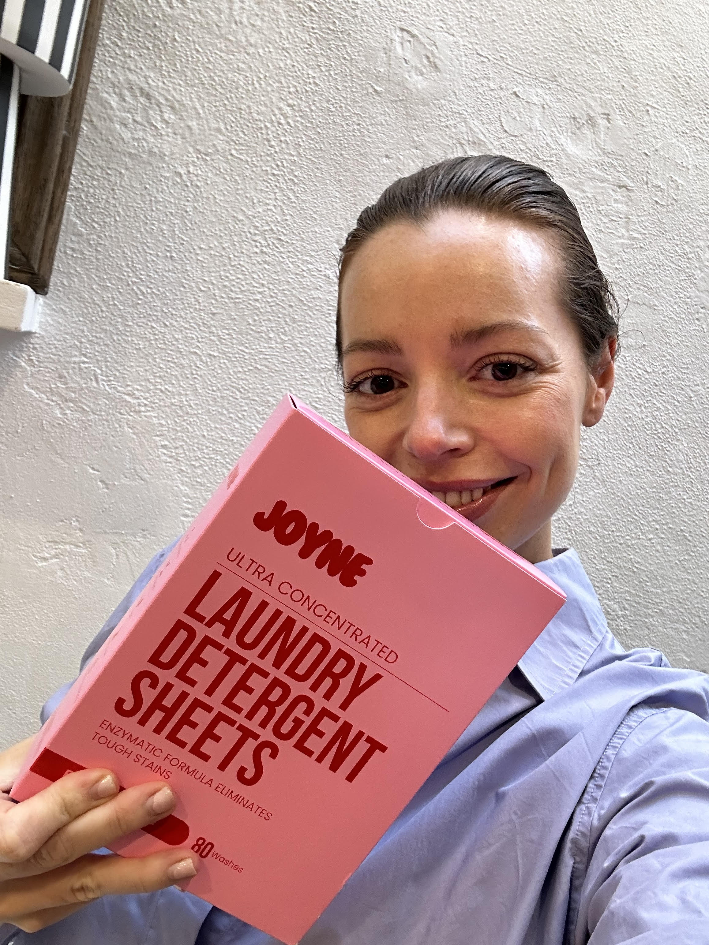 A smiling women holding a pink box of laundry detergent sheets