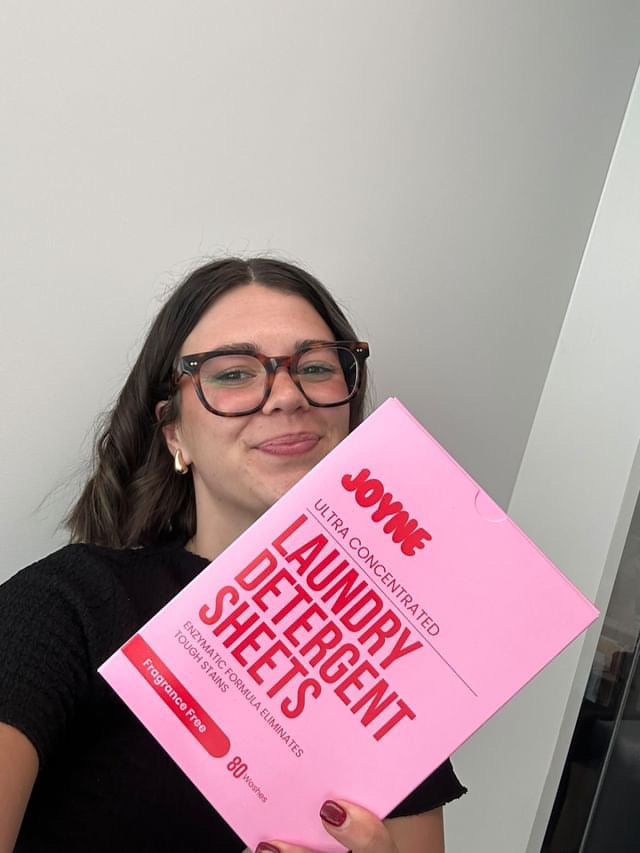 A smiling women holding a pink box of laundry detergent sheets