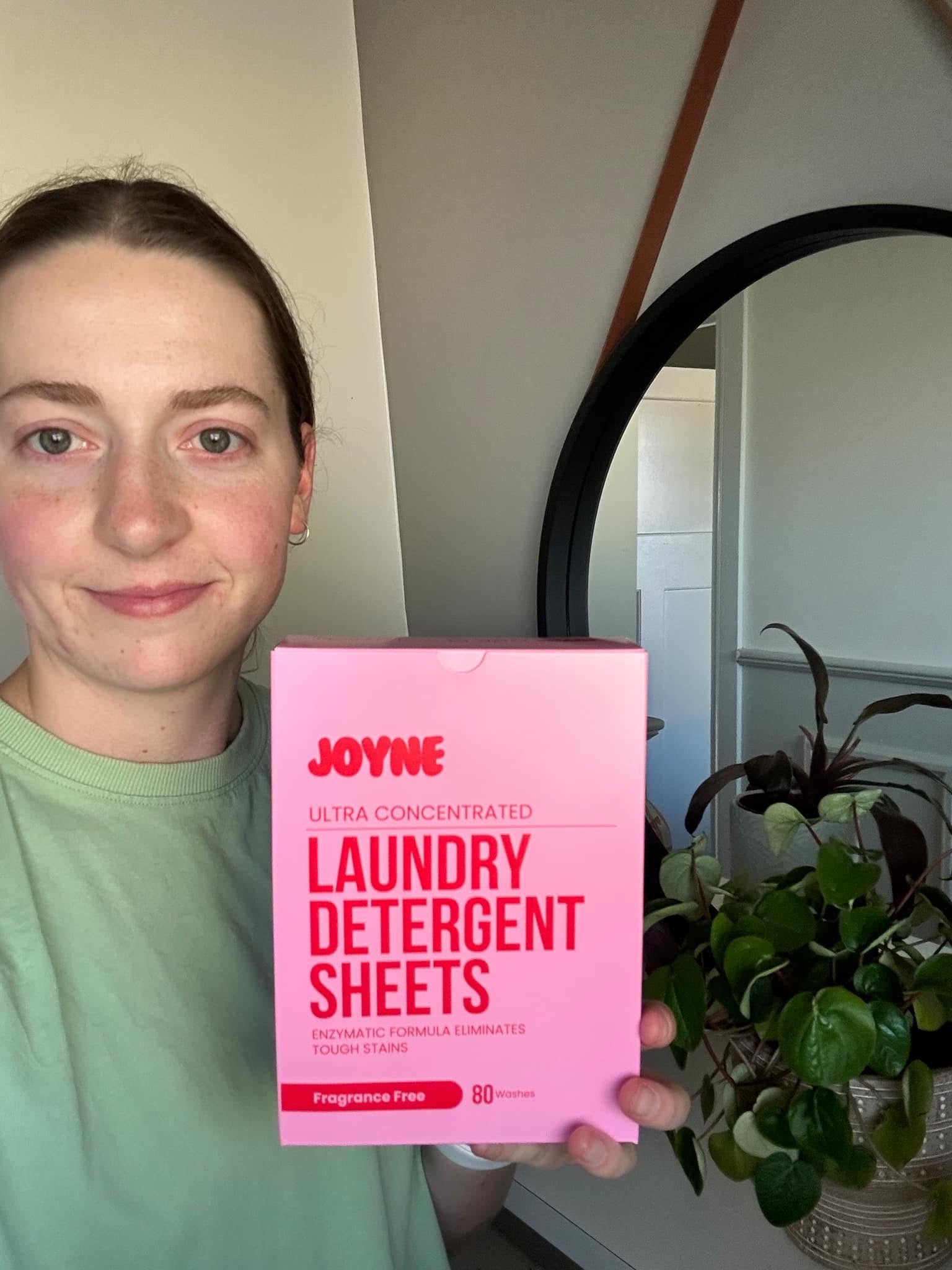 A smiling women holding a pink box of laundry detergent sheets