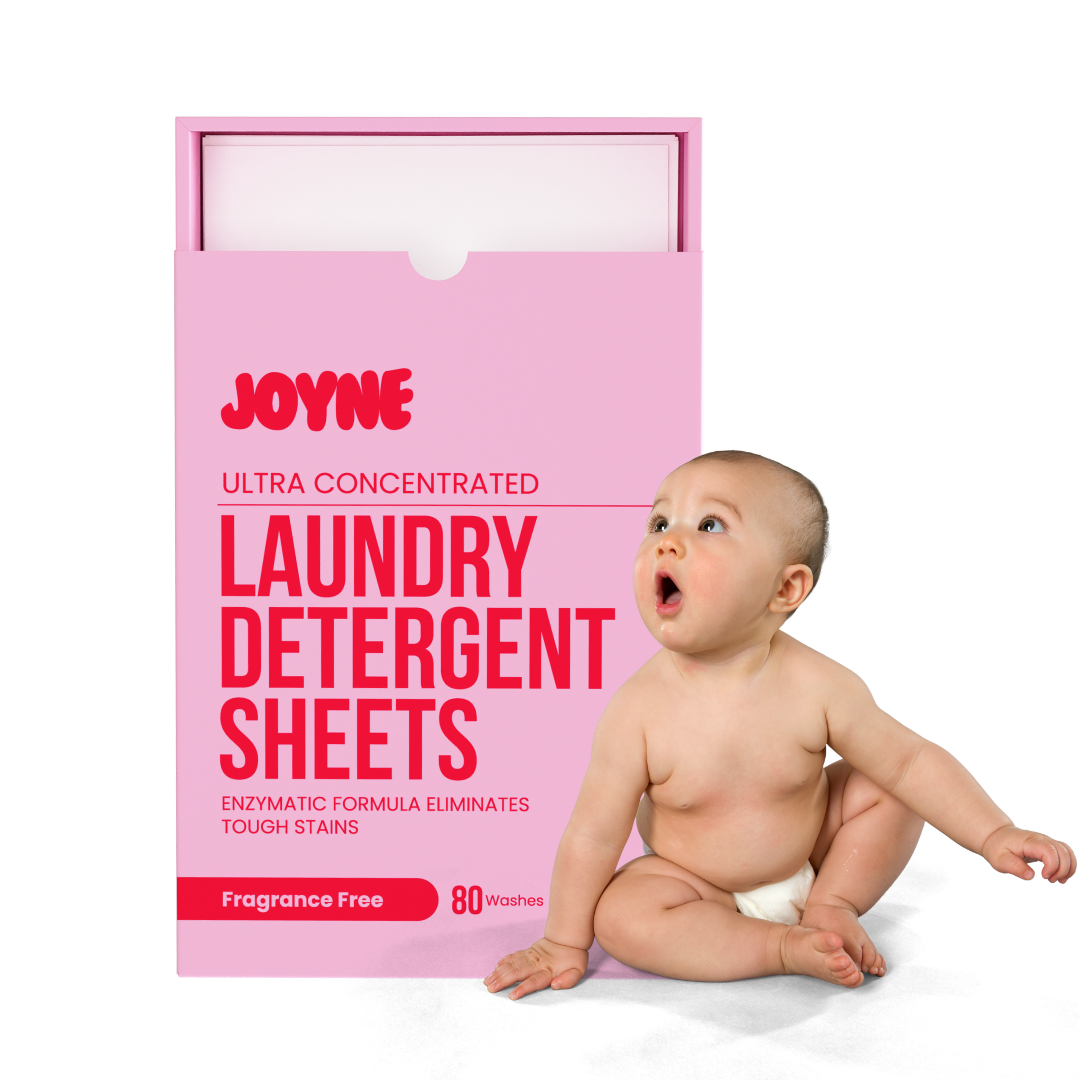 A baby sitting next to a large pink box of JOYNE laundry detergent sheets