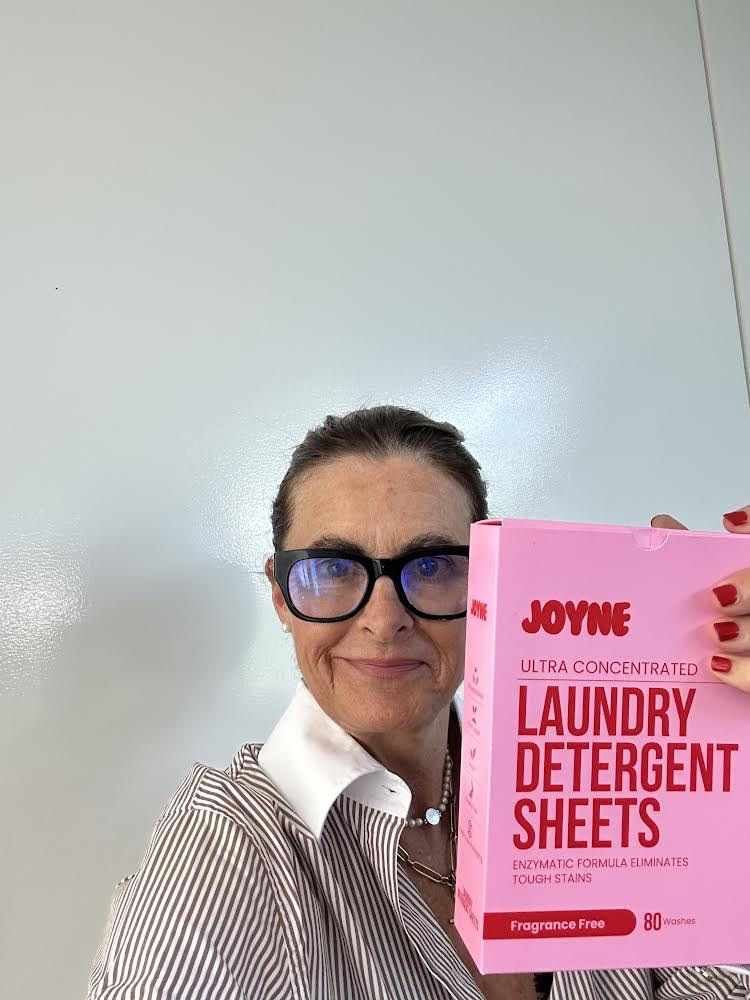 A smiling women holding a pink box of laundry detergent sheets