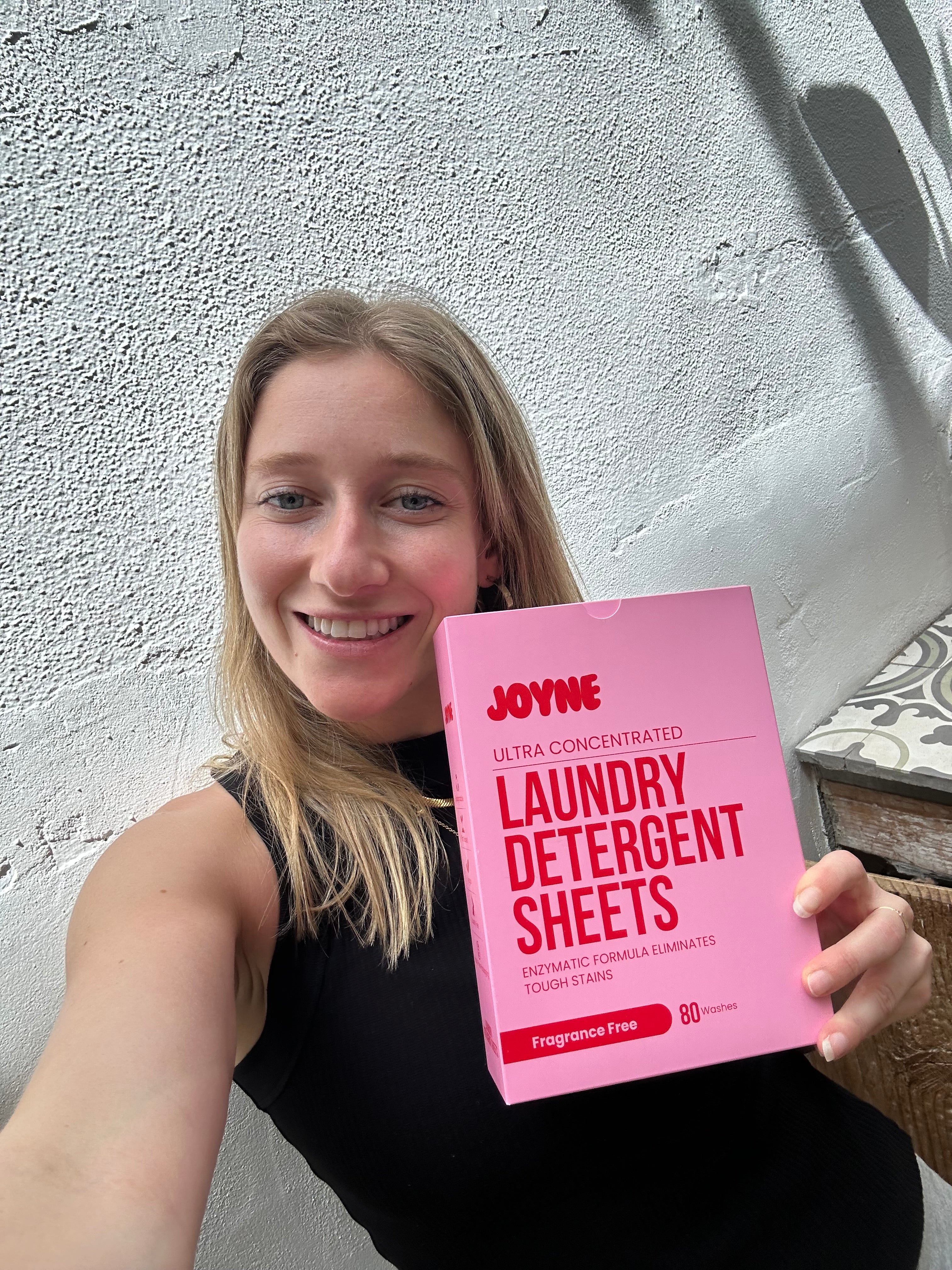 A smiling women holding a pink box of laundry detergent sheets